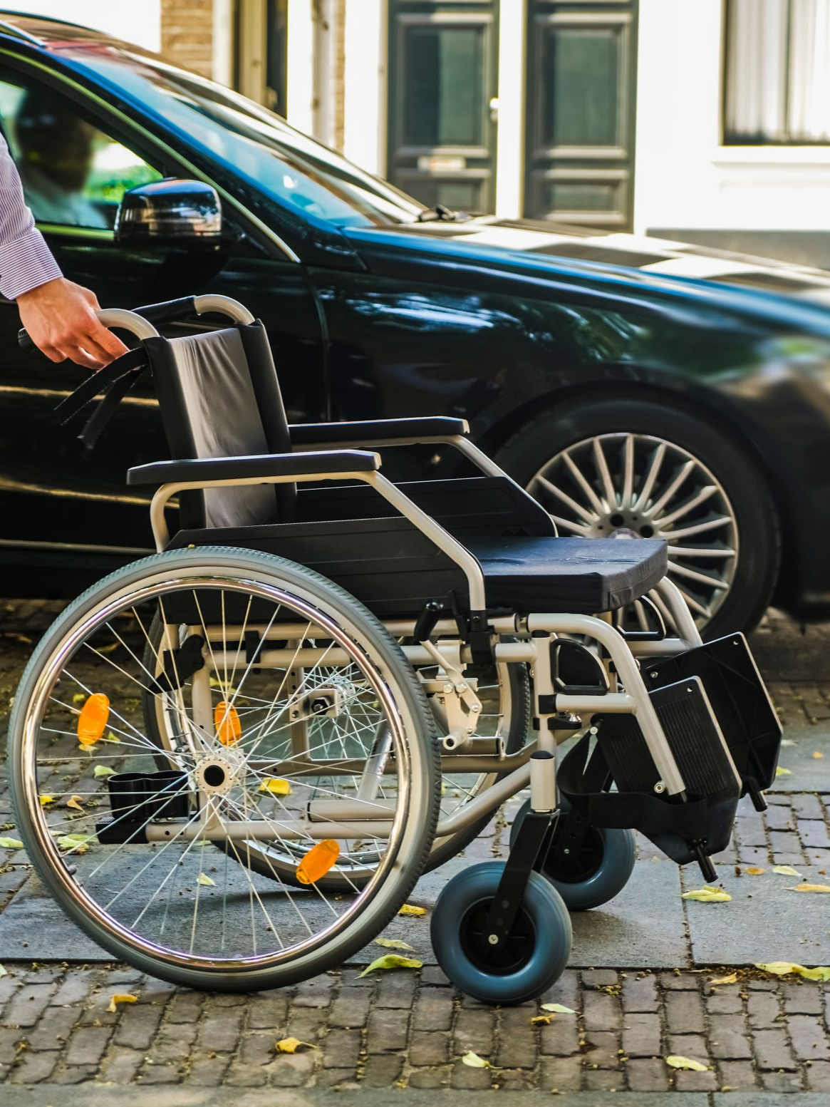 Fauteuil roulant près d'une voiture noire, personne ouvrant la portière de la voiture.