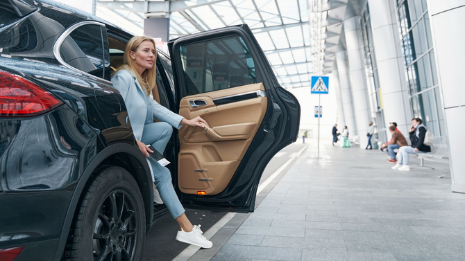Une femme sortant d'un SUV noir dans un aéroport, tenant des billets.