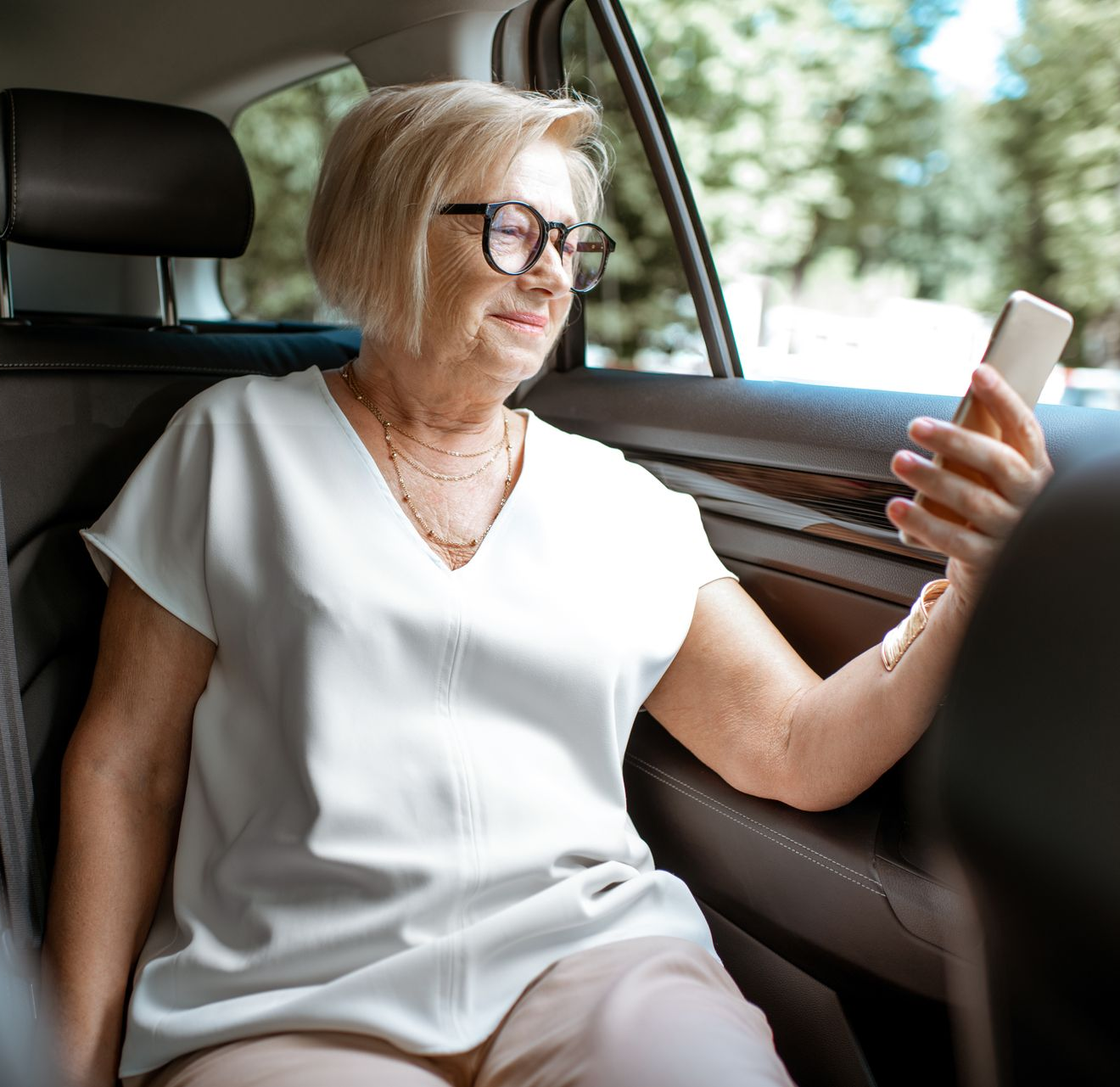 Femme en voiture, regardant son smartphone. Elle porte des lunettes et un haut blanc.
