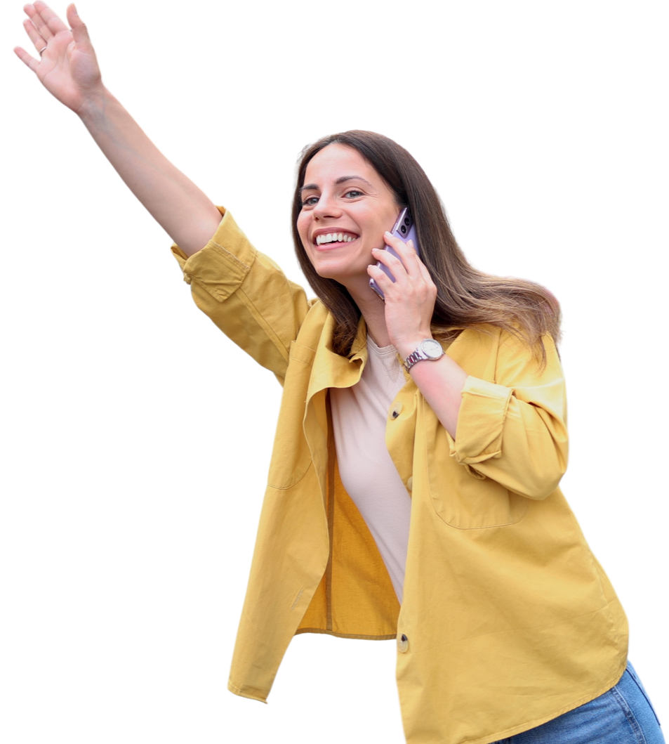 Une femme en chemise jaune fait un signe de la main, sourit et parle au téléphone.
