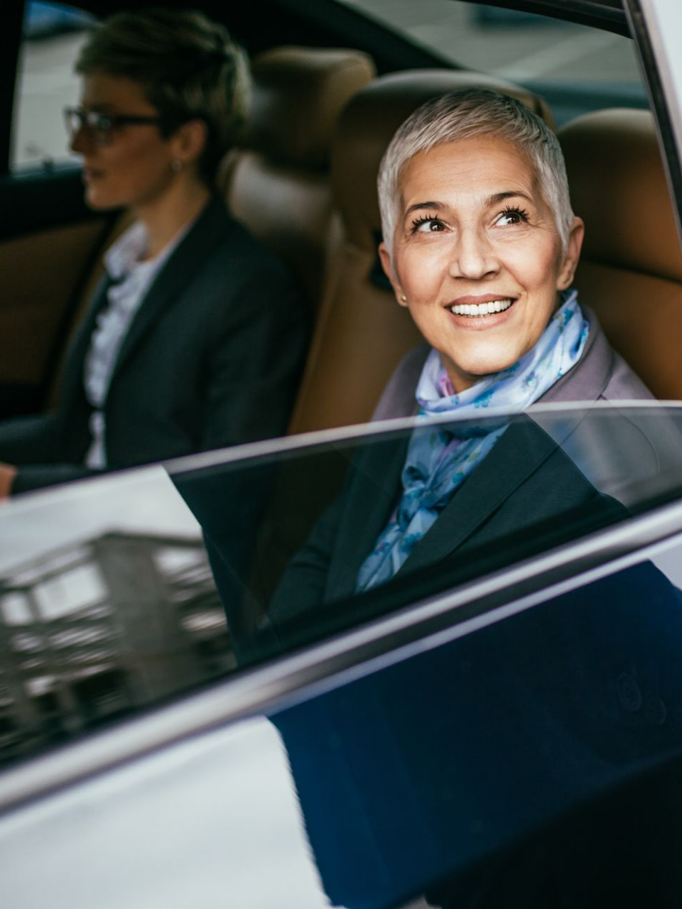 Une femme aux cheveux gris courts sourit dans une voiture, une autre femme est à côté.
