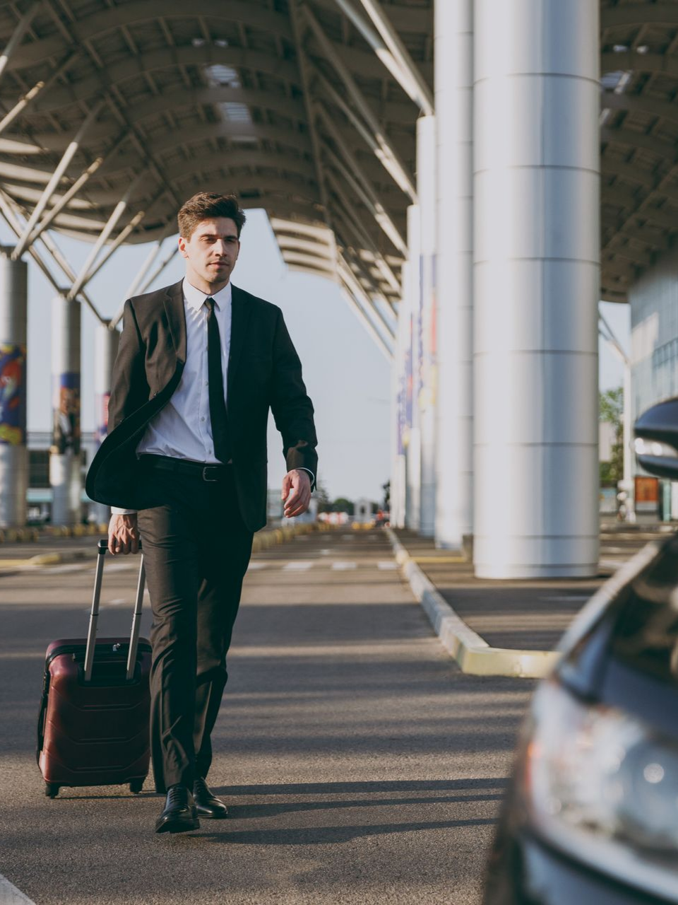Un homme en costume marchant avec des bagages près d'une voiture dans un aéroport.
