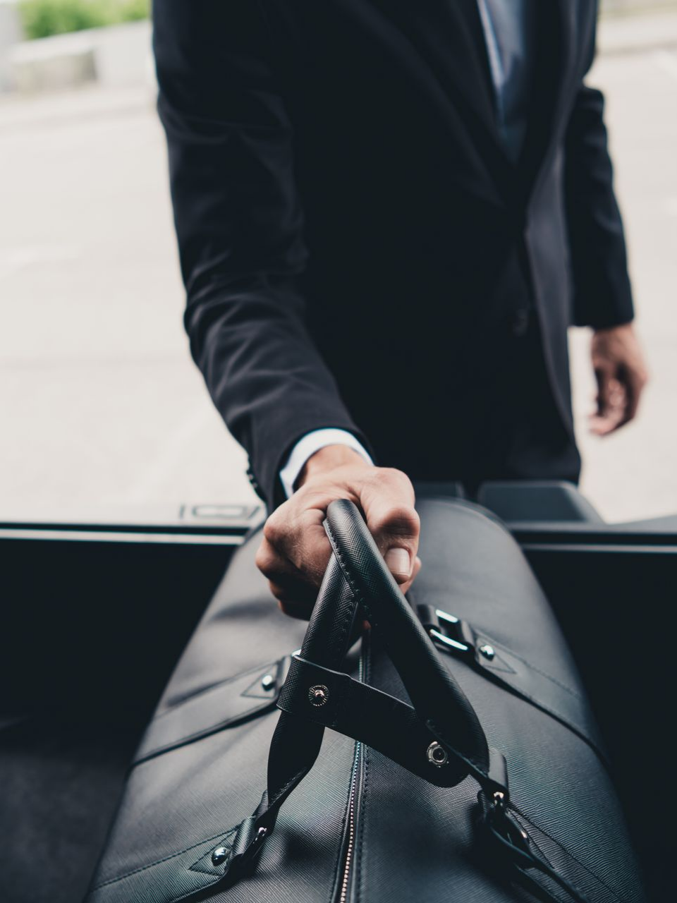 Un homme en costume sort un sac de sport en cuir noir du coffre d'une voiture.