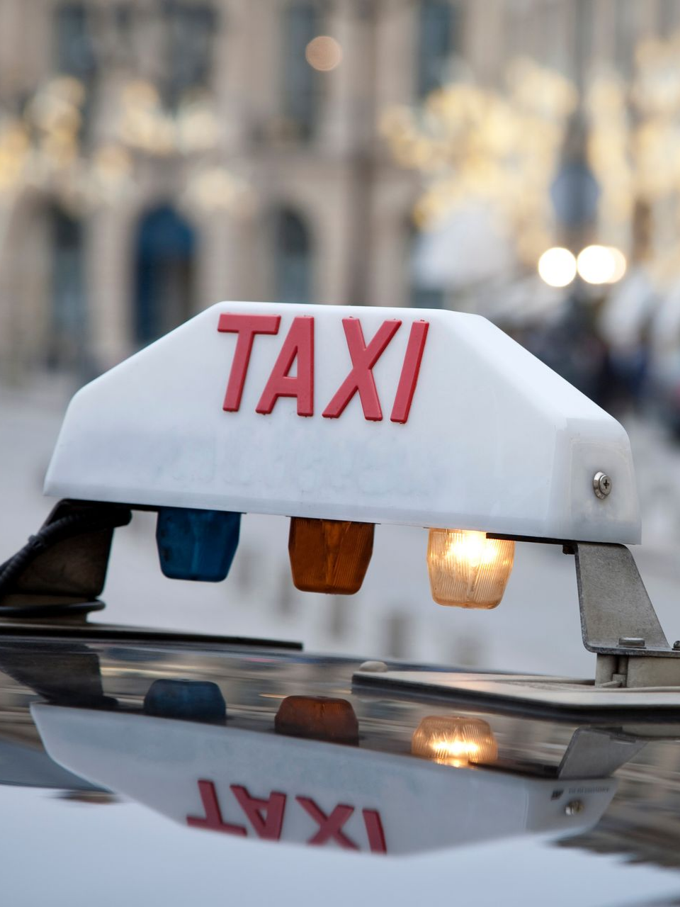 Panneau de taxi blanc avec inscription rouge TAXI et trois lumières colorées.