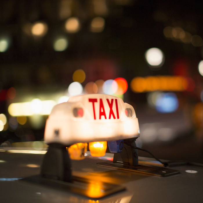 Panneau de taxi éclairé sur une voiture la nuit ; lumières floues de la ville en arrière-plan.