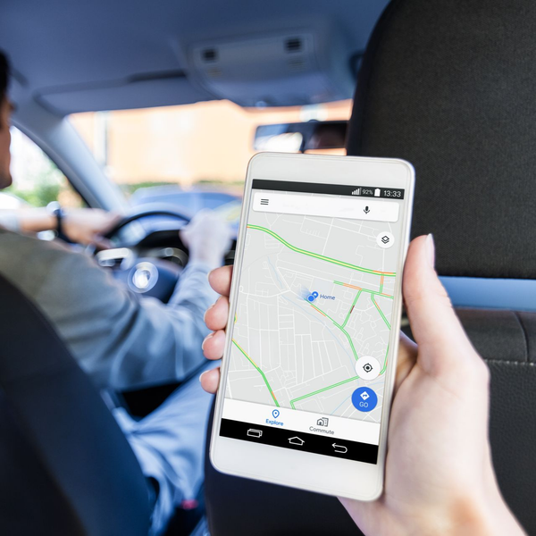Personne tenant un smartphone avec une application de carte à l'intérieur d'une voiture, conducteur en arrière-plan.