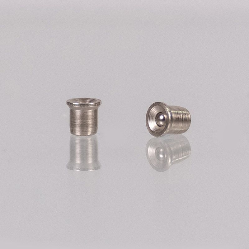 Zwei kleine, silberne Metallnieten auf einer spiegelnden Oberfläche. Eine weist eine abgerundete Spitze auf, die andere hat ein versenktes Kugellager.