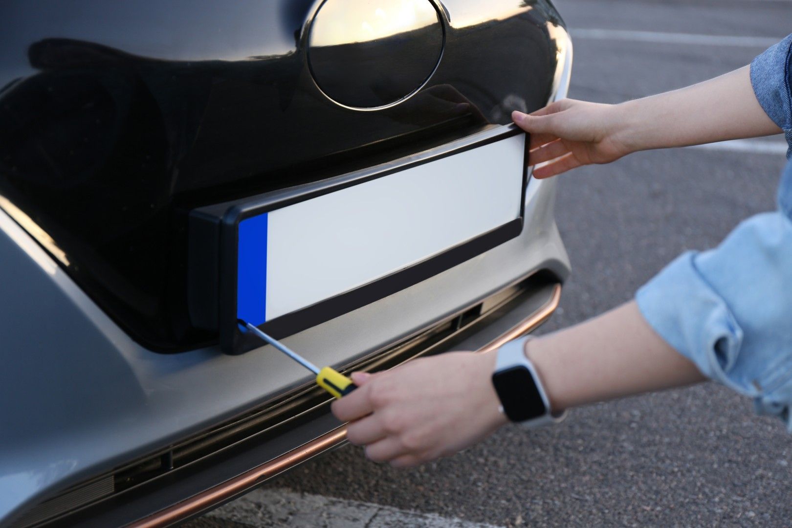 Des mains mesurant l’emplacement de la plaque d’immatriculation arrière d’une voiture à l’aide d’un mètre ruban