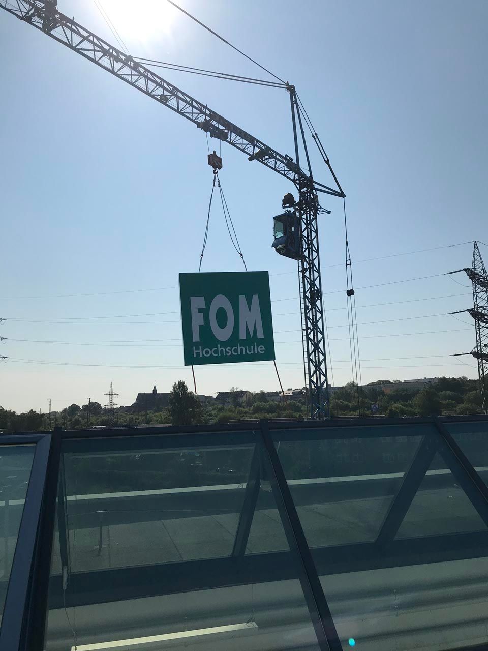 Montagearbeiten für ein FOM Schild auf einem großen Gebäude mit einem Kran.