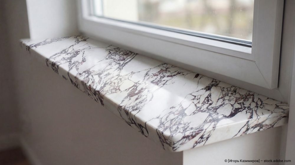 Eine Fensterbank mit Marmormuster, die in einem minimalistischen Interieur an einem weißen Fensterrahmen angebracht ist.
