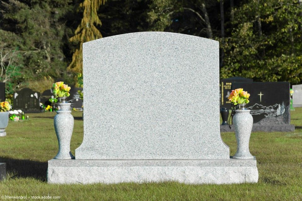 Ein grauer Granitgrabstein auf einem Friedhof mit zwei passenden Steinvasen, die gelbe Blumen enthalten, auf seinem Sockel.