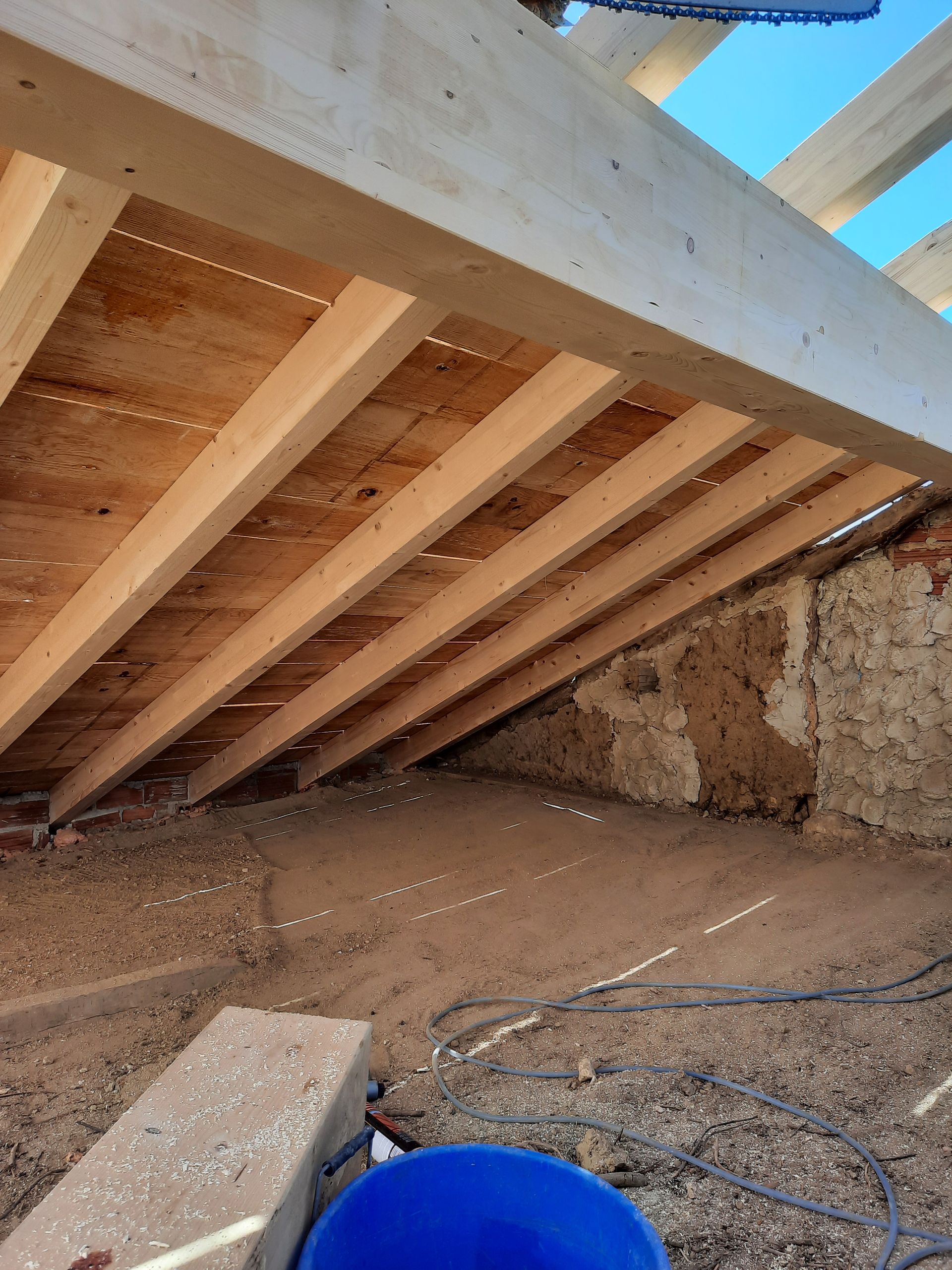 Ático con vigas y tablones de madera, suelo polvoriento, pared de piedra.