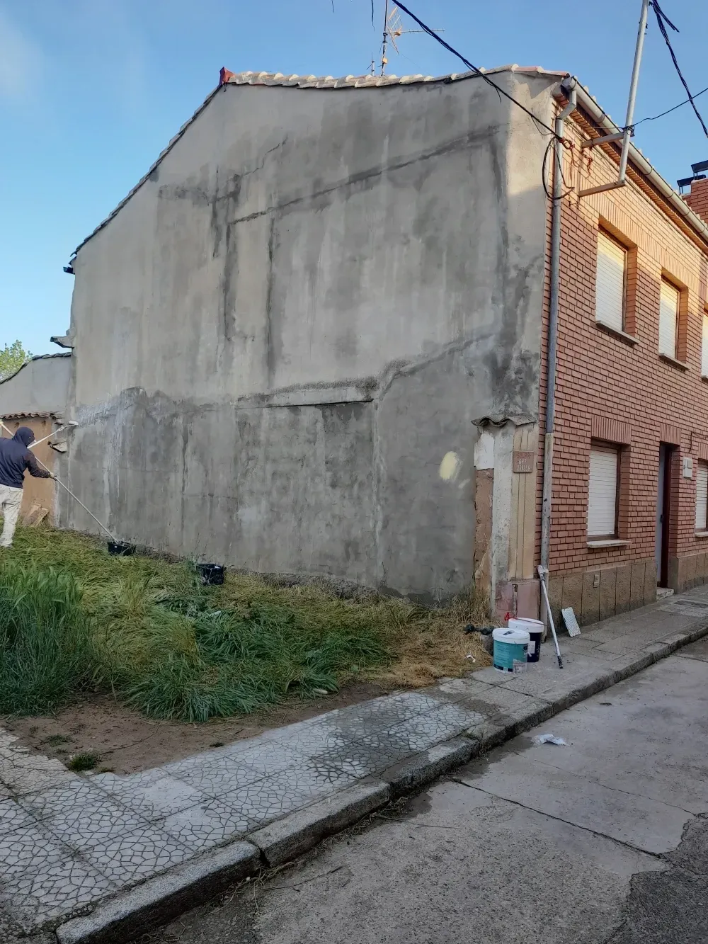 Lateral de un edificio de ladrillo y una pared de estuco. Una persona rocía una sustancia sobre la pared.