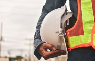 Ouvrier avec gilet jaune et orange tenant un casque de chantier blanc