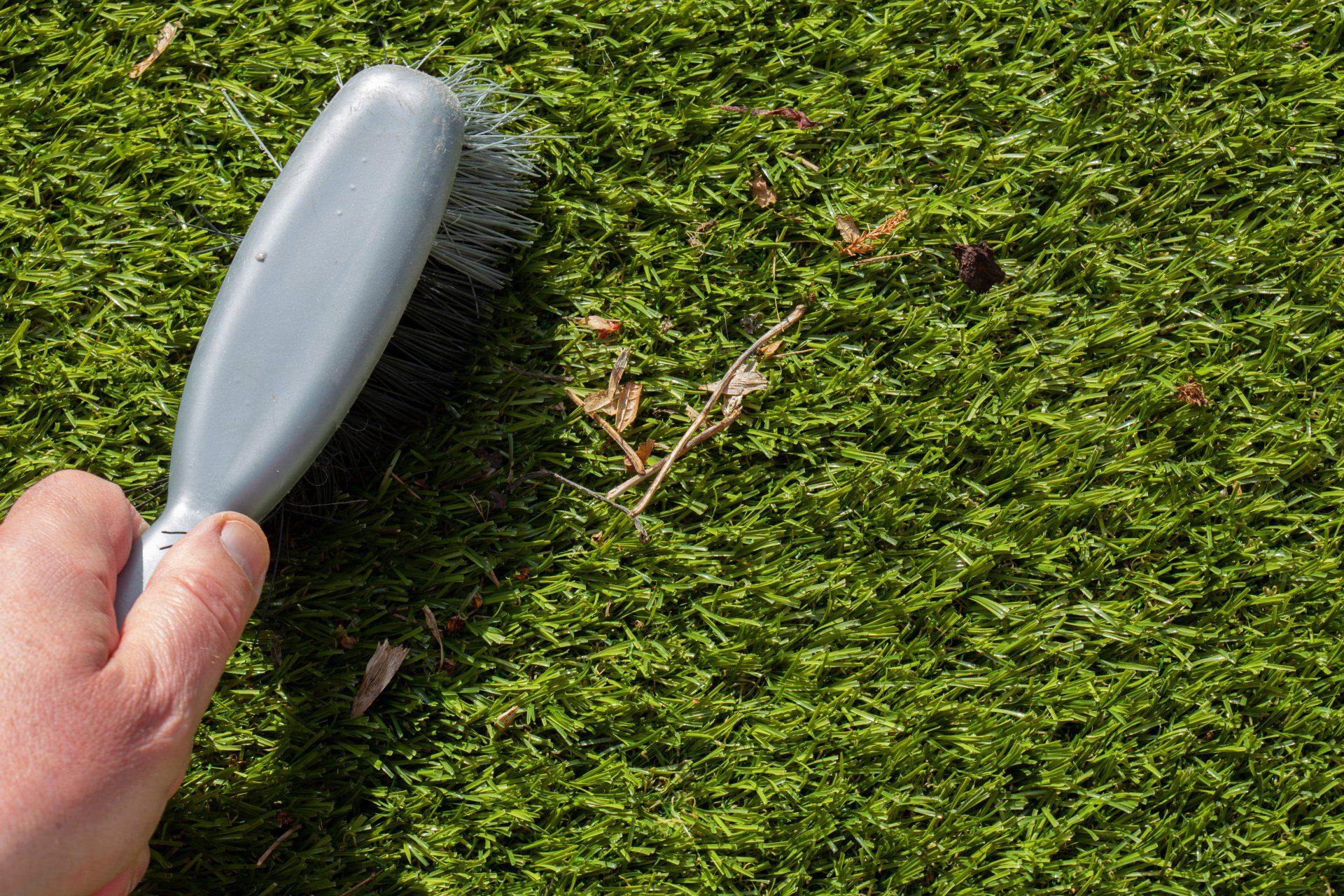 Une personne utilise une brosse pour nettoyer les feuilles mortes et les débris d'une parcelle de gazon artificiel.