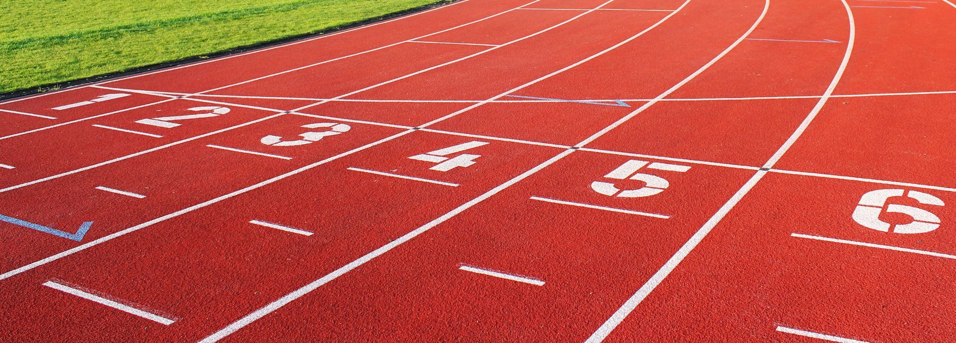 Piste d'athlétisme rouge avec marquages et numéros de couloirs blancs, serpentant autour d'un champ vert