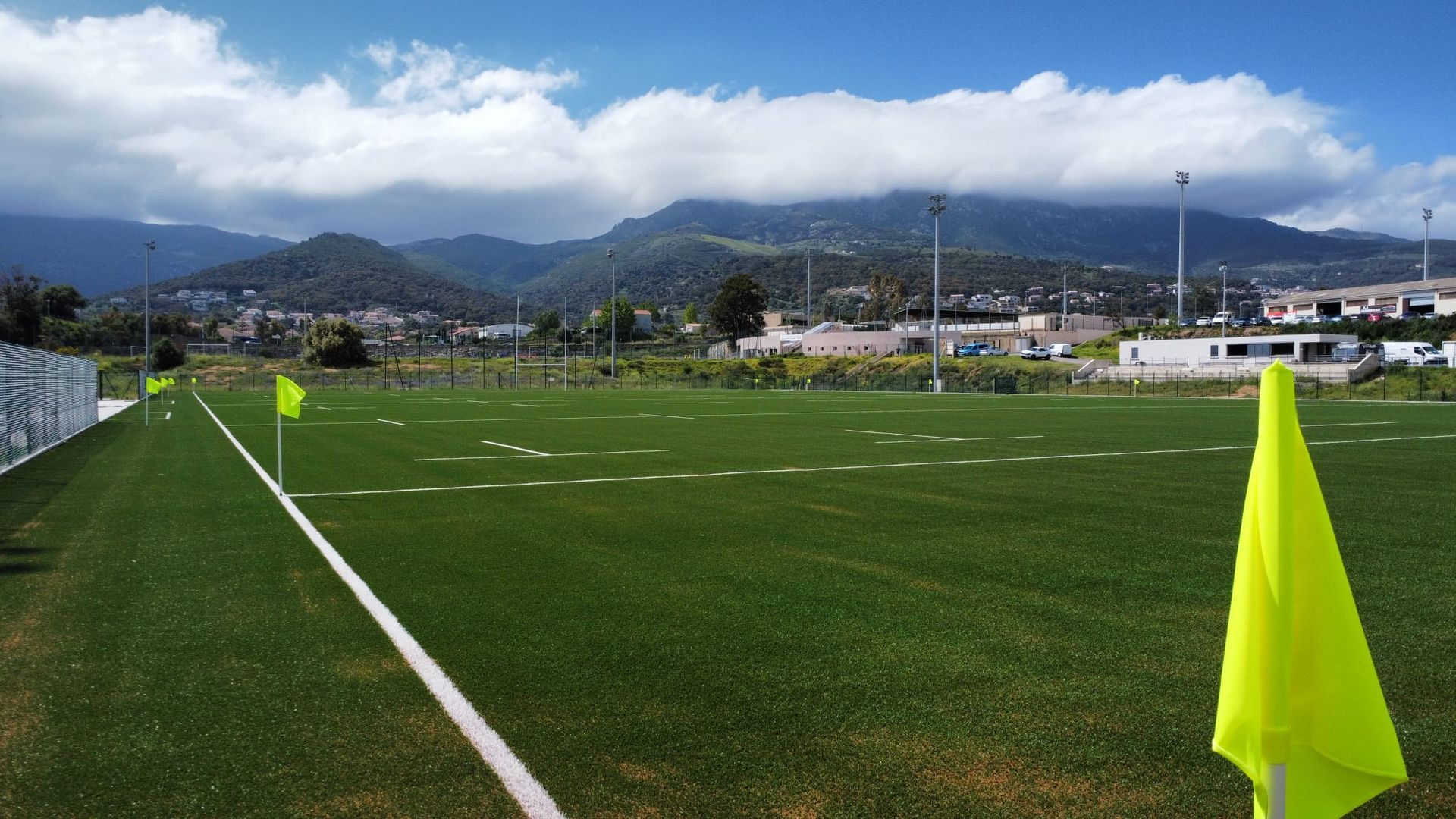 Terrain de football avec des drapeaux de coin vert vif et des montagnes en arrière-plan sous un ciel nuageux