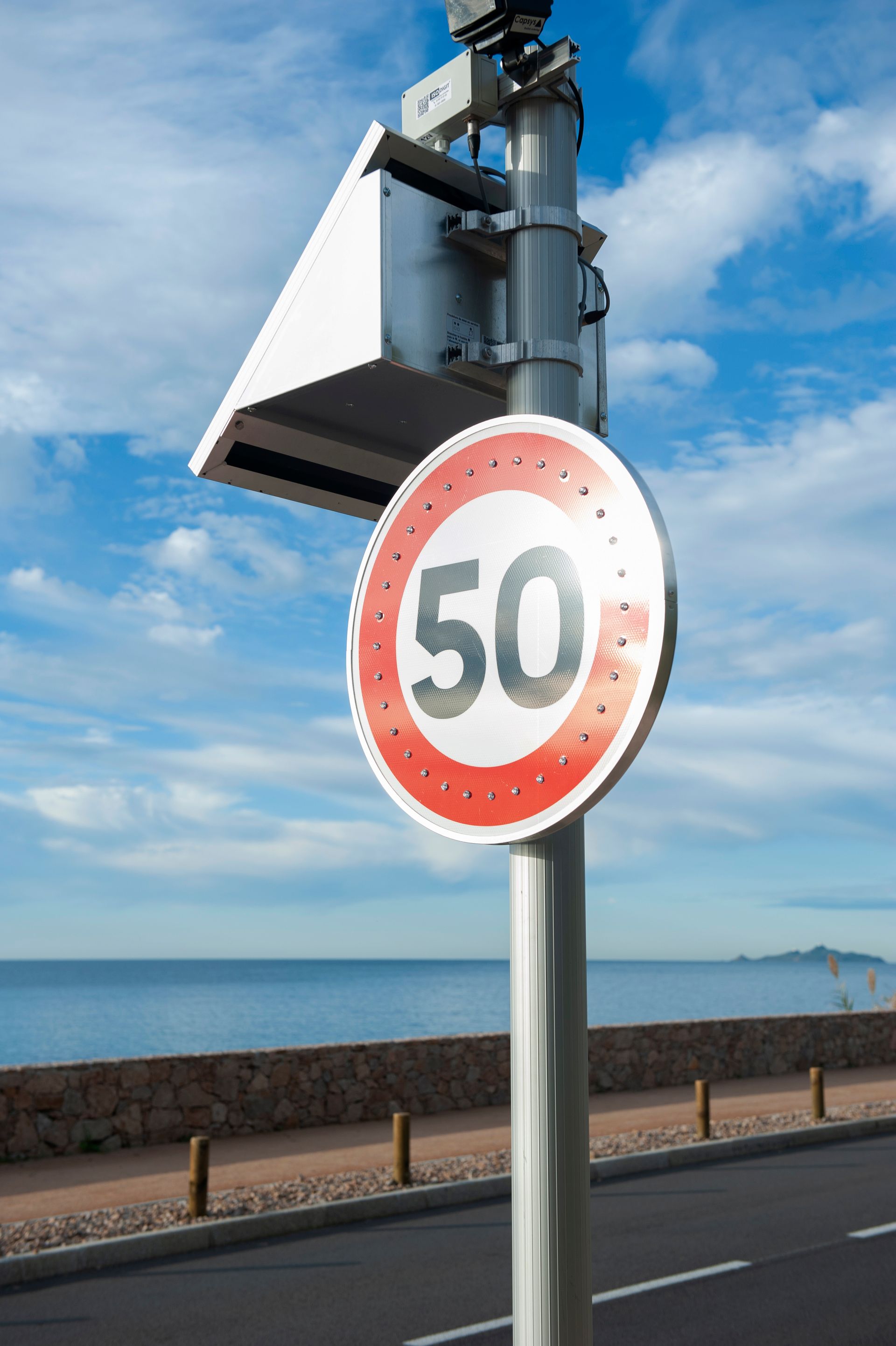 Panneau de limitation de vitesse à 50 sur une route côtière avec ciel bleu et vue sur l'océan