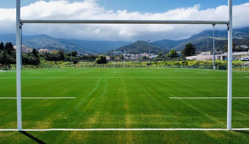 Cadre de but de football donnant sur un terrain verdoyant avec des montagnes et un ciel nuageux en arrière-plan