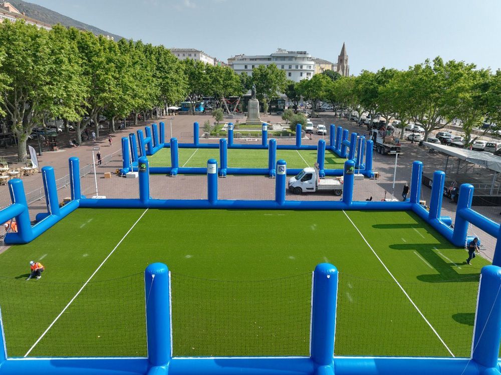 Deux terrains de football gonflables bleus sur une place pavée, vus d'un point de vue surélevé.