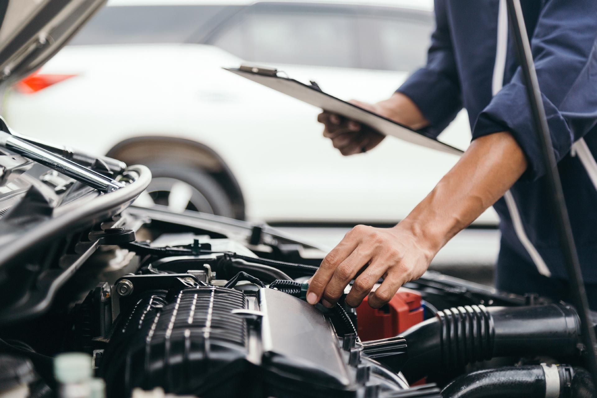 Ein Mechaniker untersucht mit einem Klemmbrett im Freien in der Nähe eines weißen Fahrzeugs einen Automotor.
