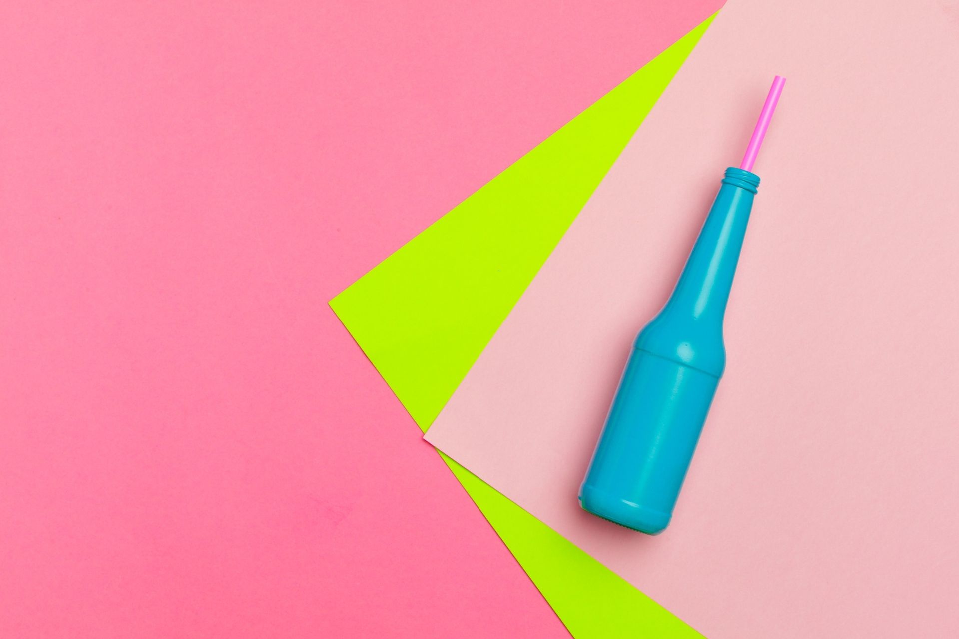 Una botella azul con una pajita rosa sobre un fondo rosa y verde.