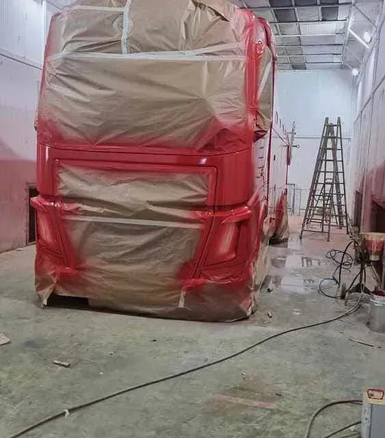 Un autobús rojo está cubierto con film plástico en un garaje.
