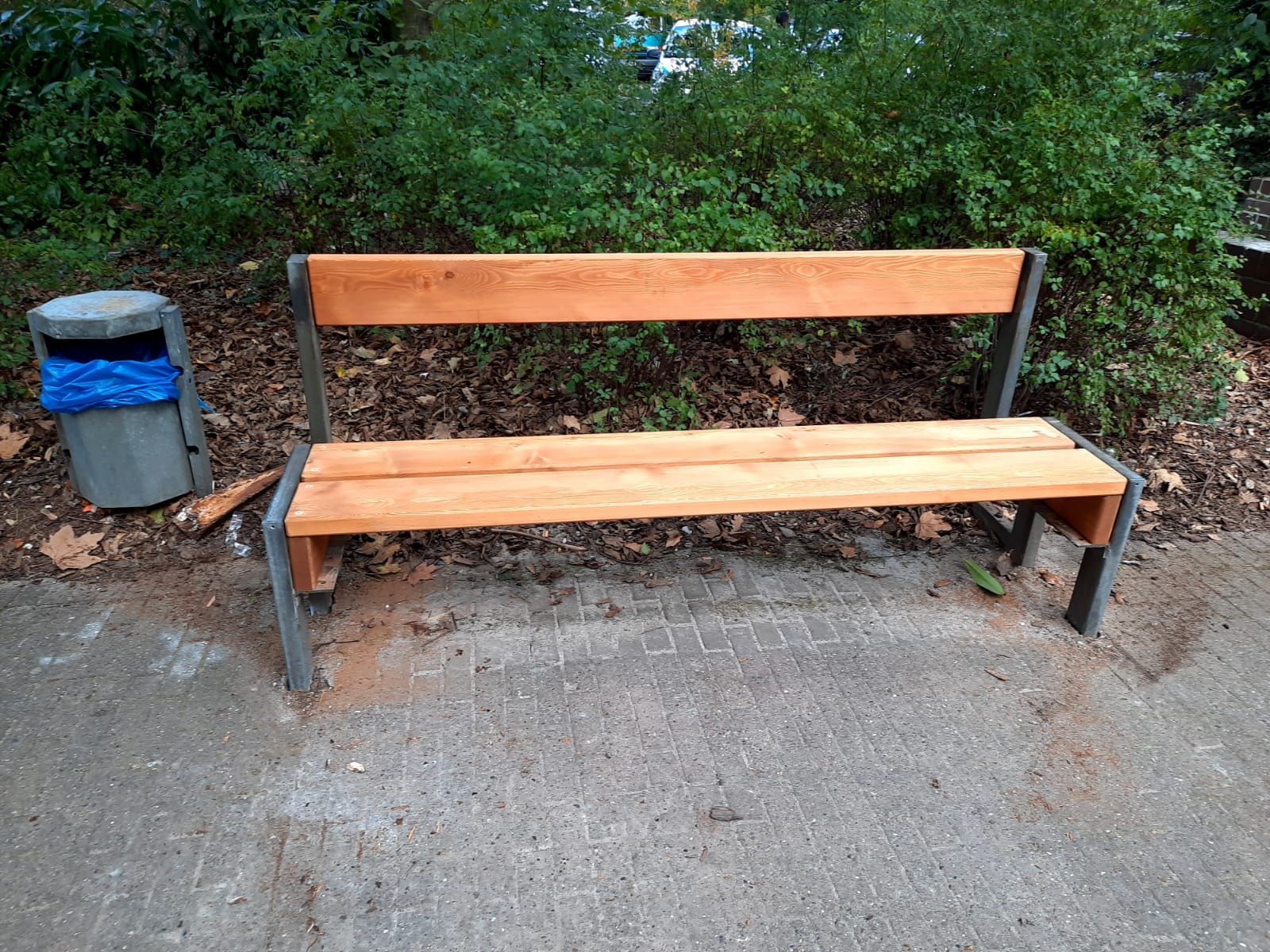 eine Holzbank sitzt neben einem Mülleimer