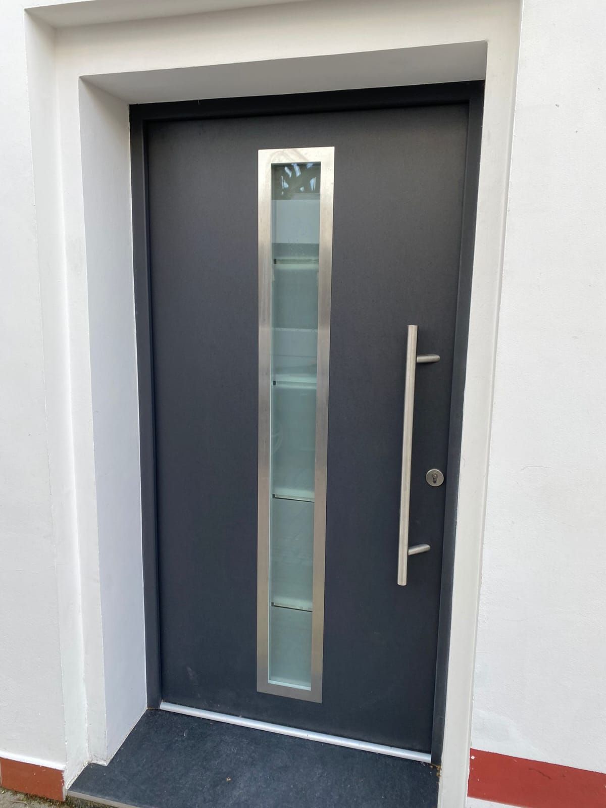 eine graue Haustür mit einem Fenster und einem Edelstahlgriff