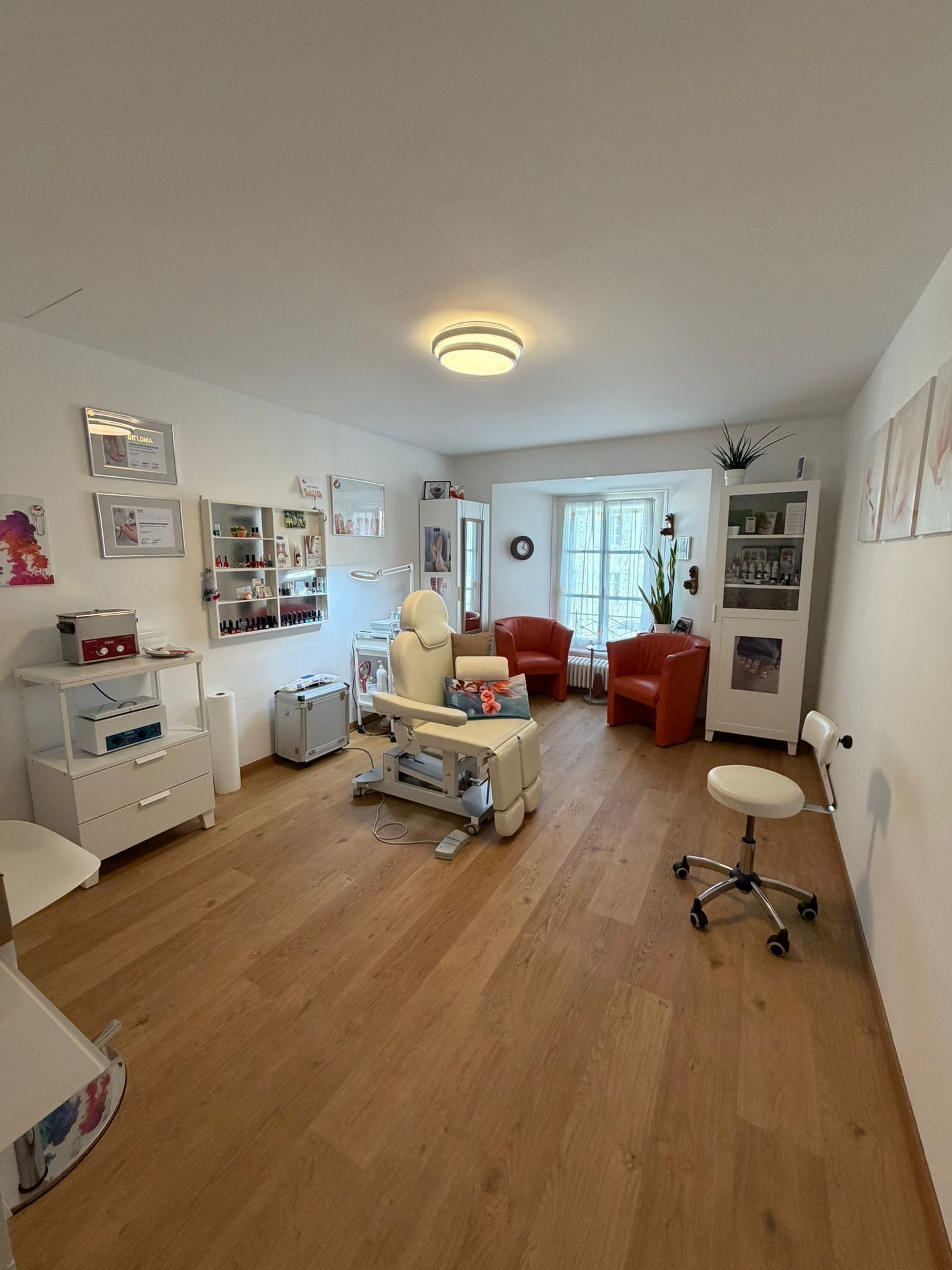 Chambre lumineuse avec matériel médical, un lit, des meubles blancs et une chaise rouge sur parquet