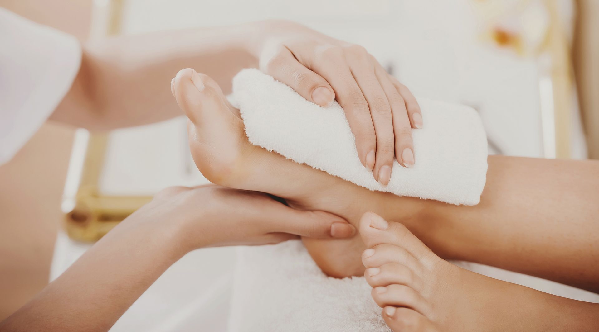 Des mains enroulant une serviette blanche autour d'un pied lors d'un massage au spa