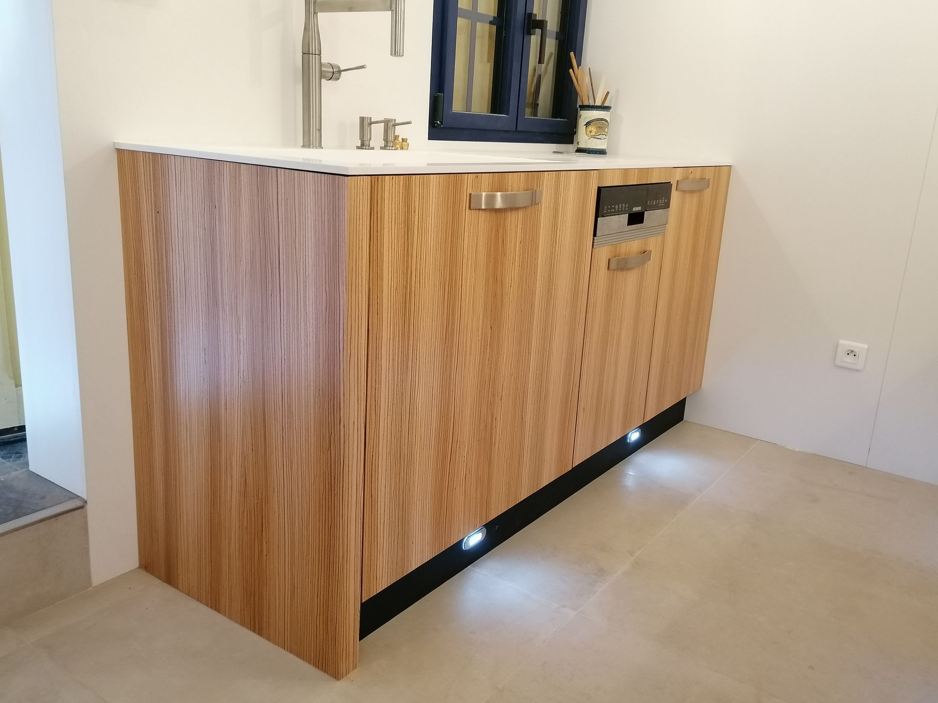 Meubles de cuisine esprit bois zébrano et corian blanc, avec un évier et un lave-vaisselle