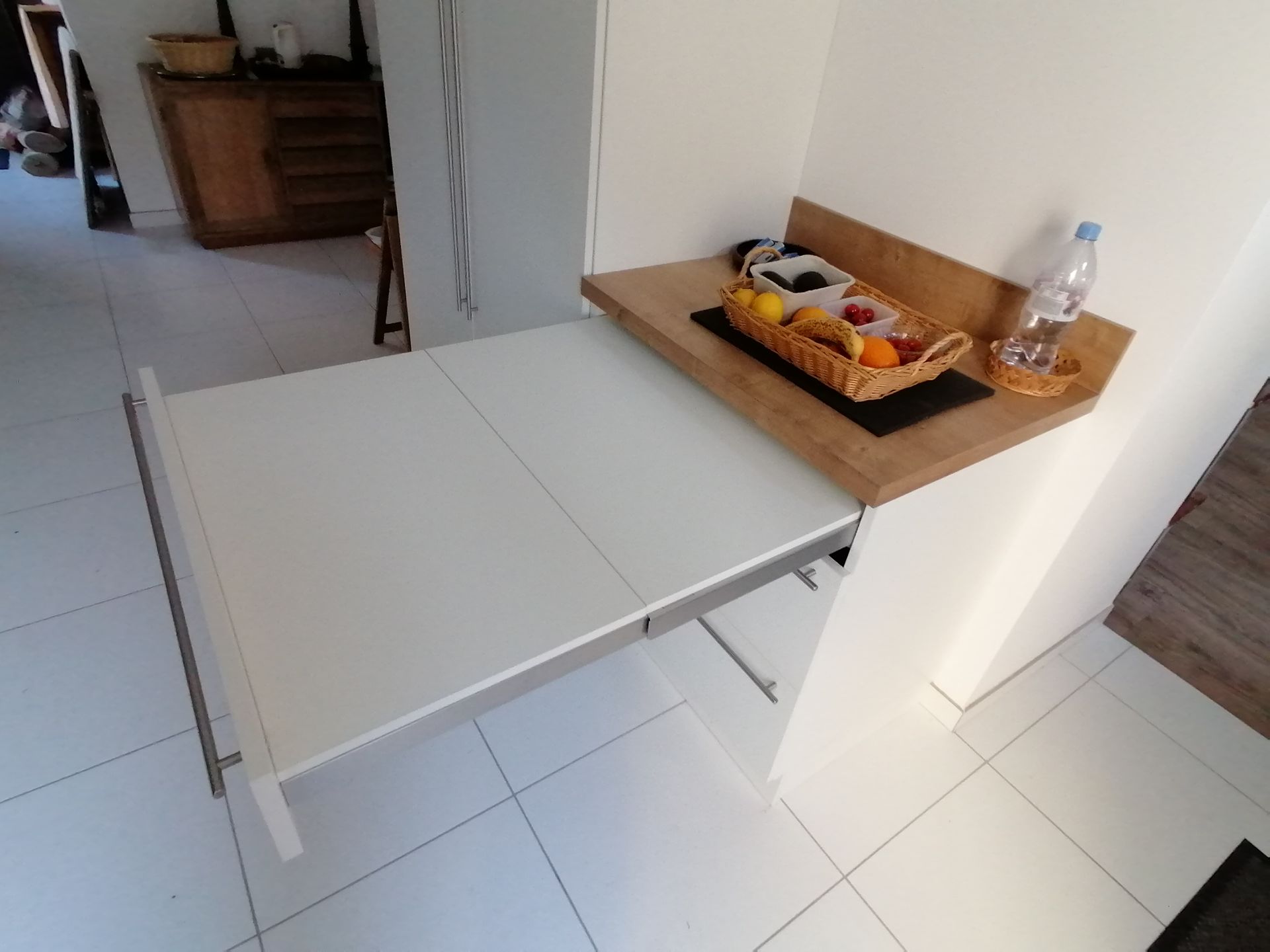 Zoom sur le meuble blanc avec des tiroirs et le plan de travail boisé : le premier tiroir s'étire pour offrir une table sans pied