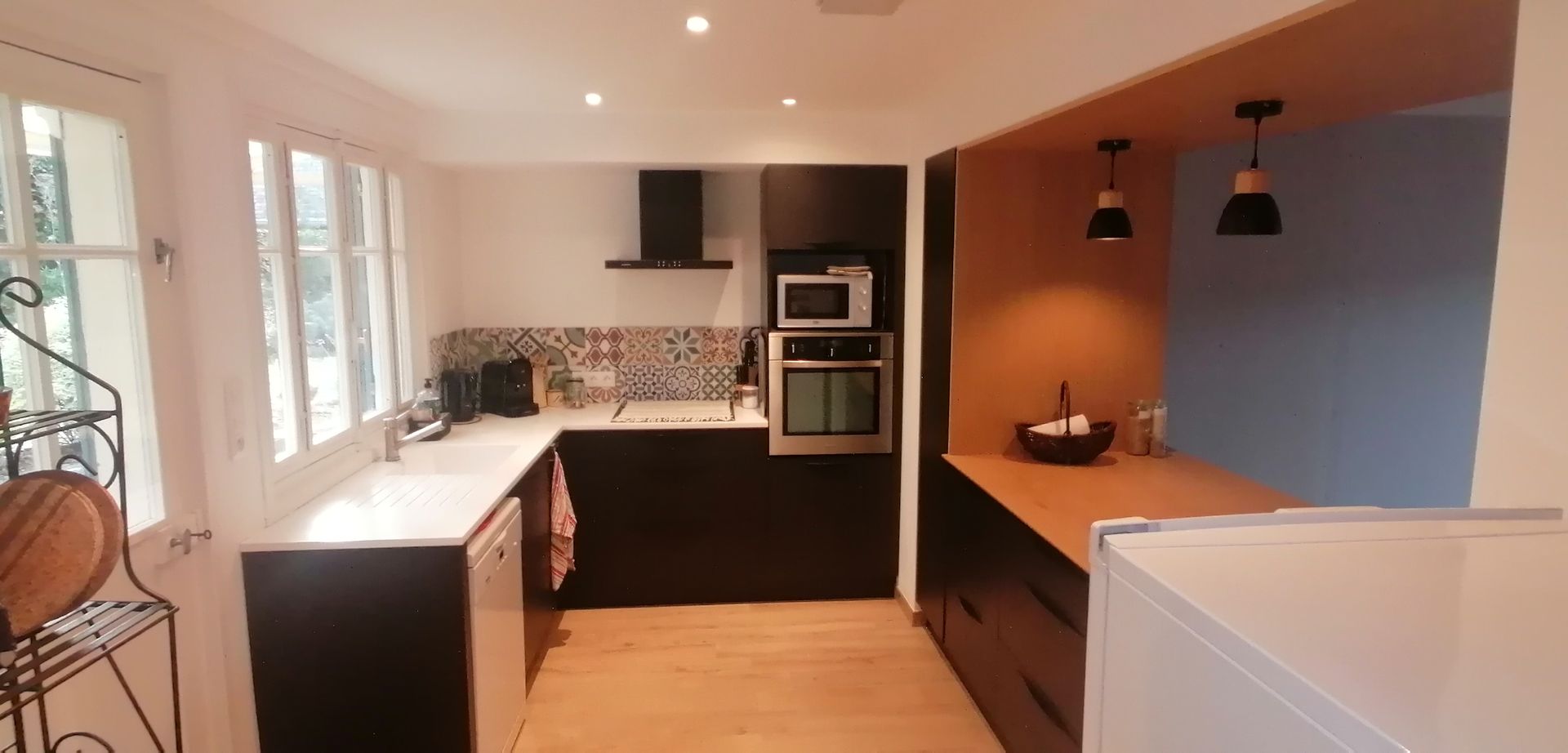 Cuisine sur mesure avec des façades noires, un plan de travail blanc et une table en chêne