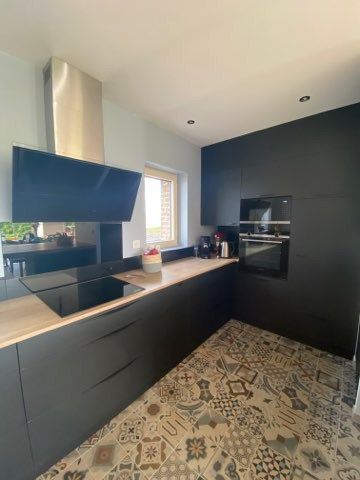 Cuisine sur mesure avec façade noire et plan de travail boisé, avec de hauts placards disposant d'un rangement pour le four