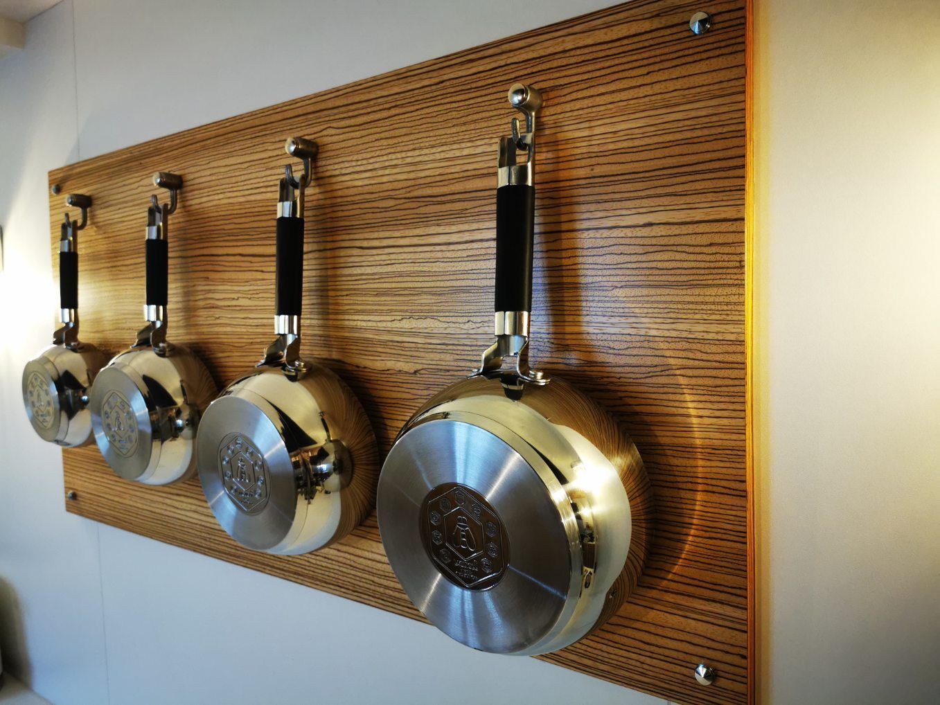 Planche accrochée au mur avec plusieurs crochets pour y installer les casseroles