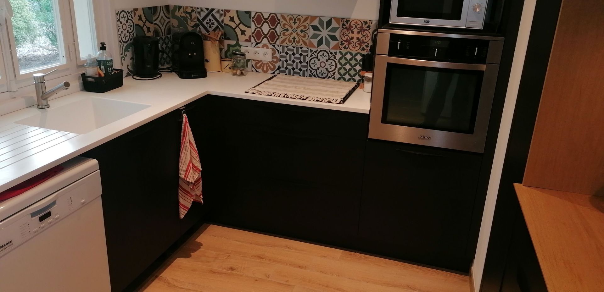 Cuisine sur mesure avec des façades noires, un plan de travail blanc et une table en chêne