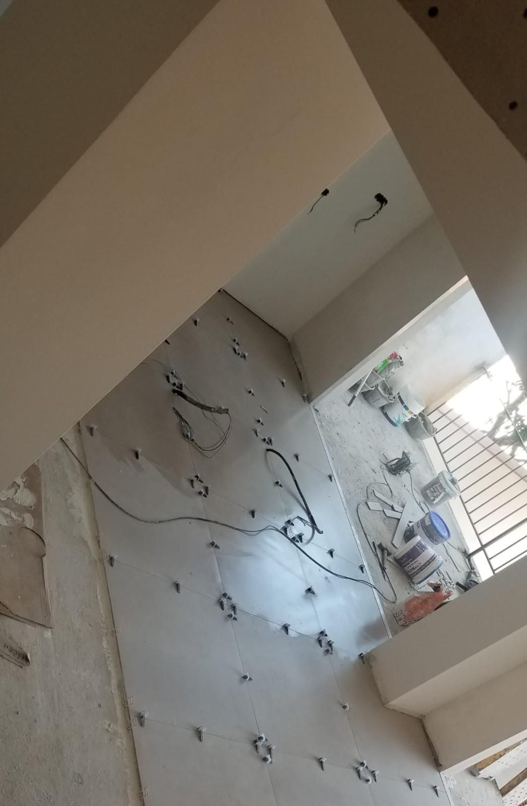 Un obrero de la construcción, con casco, transporta una viga de madera cerca de una escalera en una habitación luminosa.