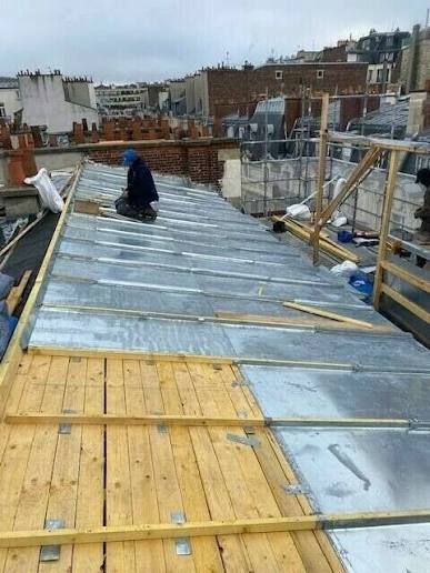 Toiture en construction avec tôles métalliques, charpente en bois et un ouvrier agenouillé au centre.