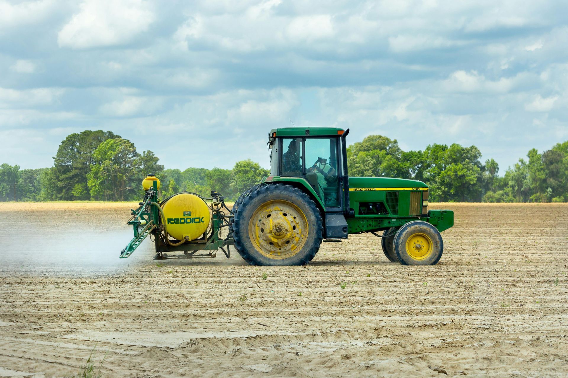 Tractor verde rociando un campo, cielo nublado.