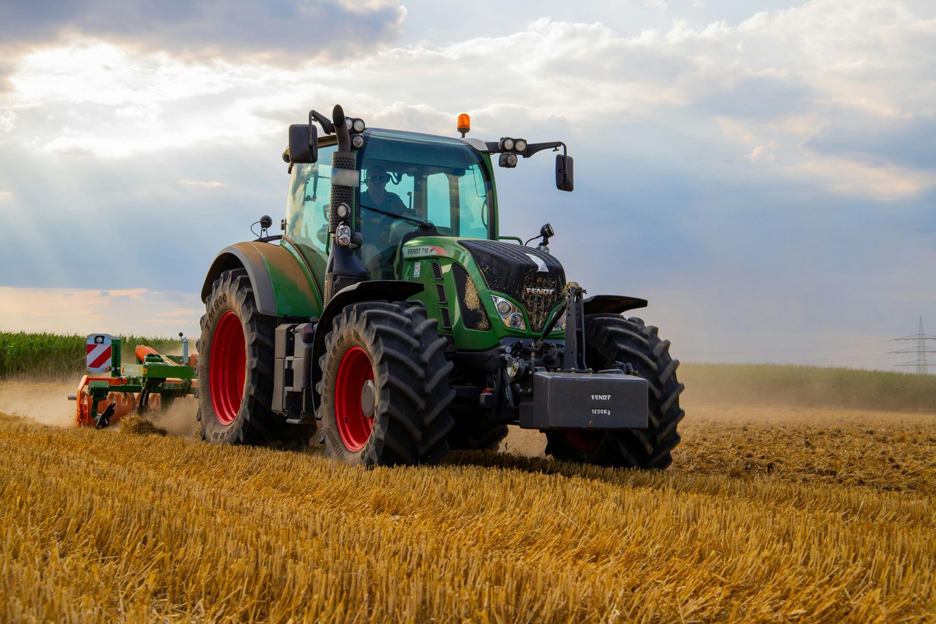 Tractor verde arando un campo, levantando tierra bajo un cielo nublado.