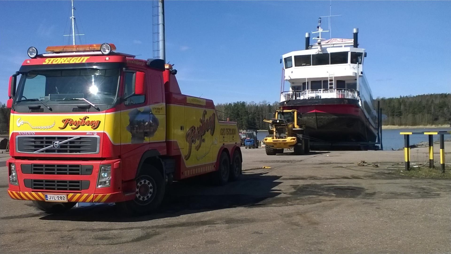 Punainen hinausauto lauttarampin vieressä, taustalla laiva laiturilla.