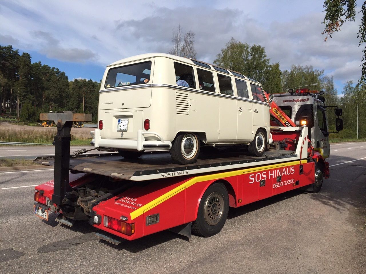 Kermanvärinen VW-pakettiauto punaisella hinausautolla tien varrella pilvisen taivaan alla