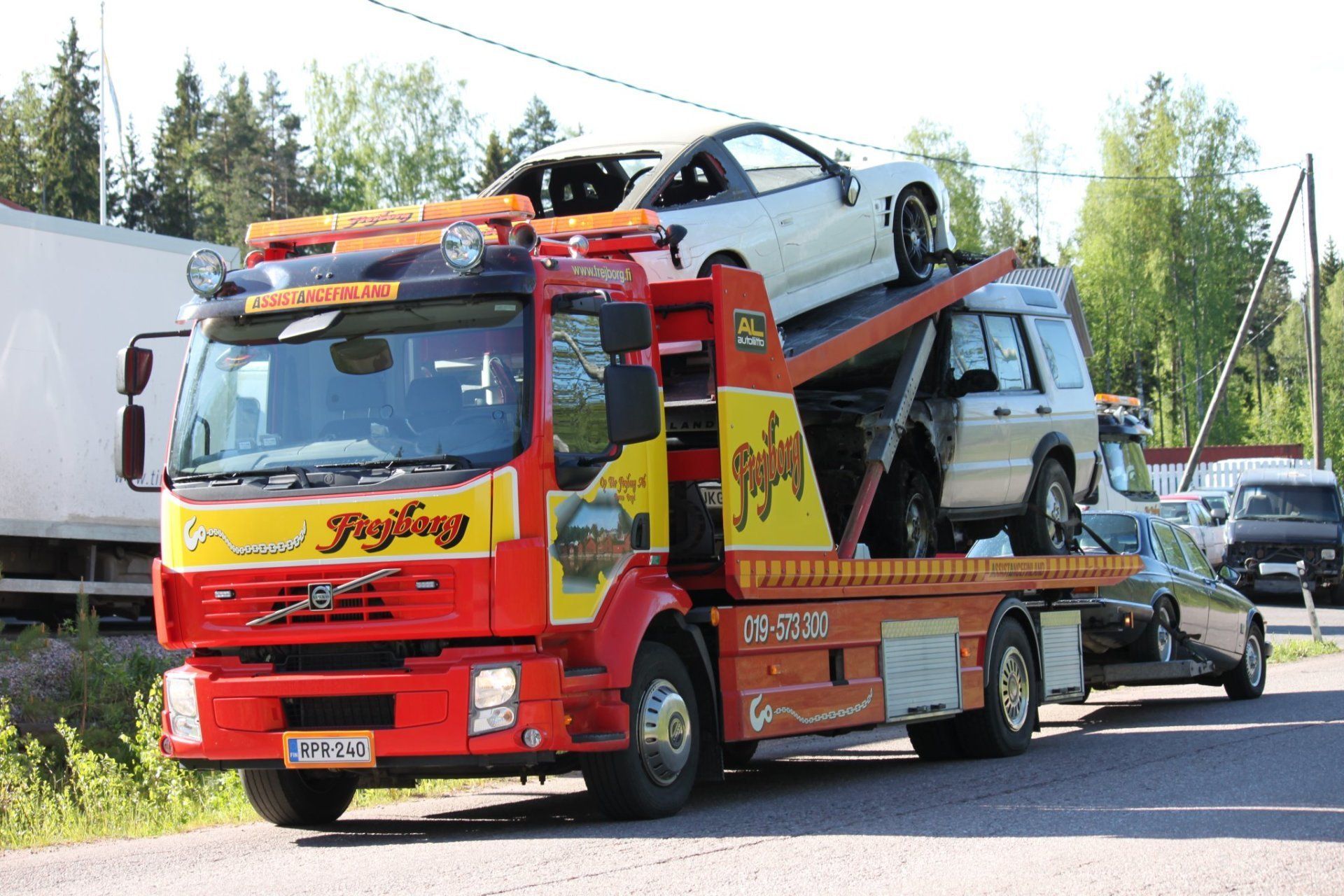 Punainen hinausauto vetää kahta autoa tiellä
