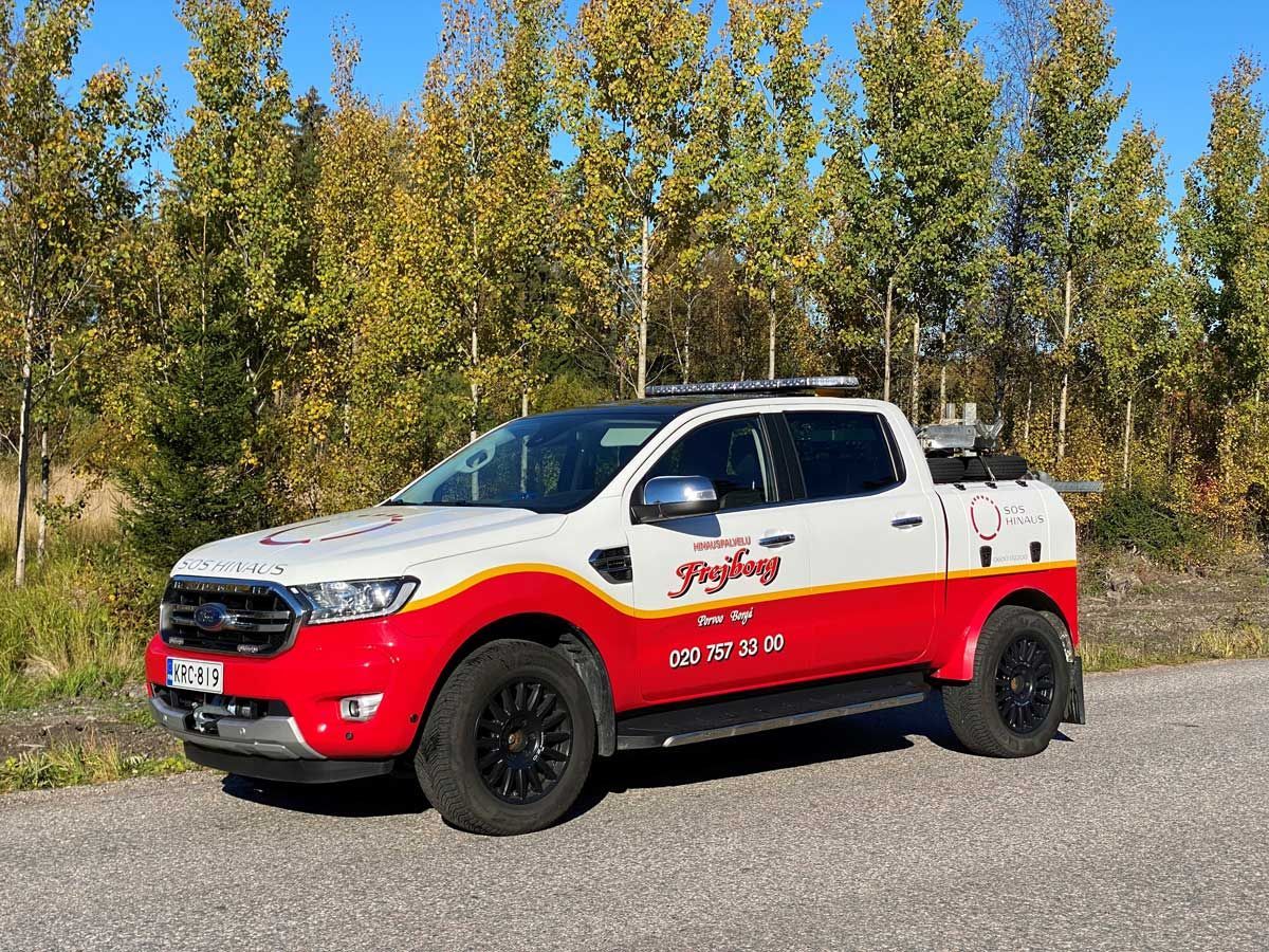 Punavalkoinen lava-auto pysäköitynä tien varteen puita taustalla.