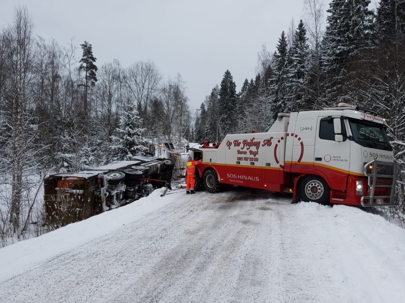 Punainen säiliöauto lumisella tiellä metsäisen rinteen vieressä talvella