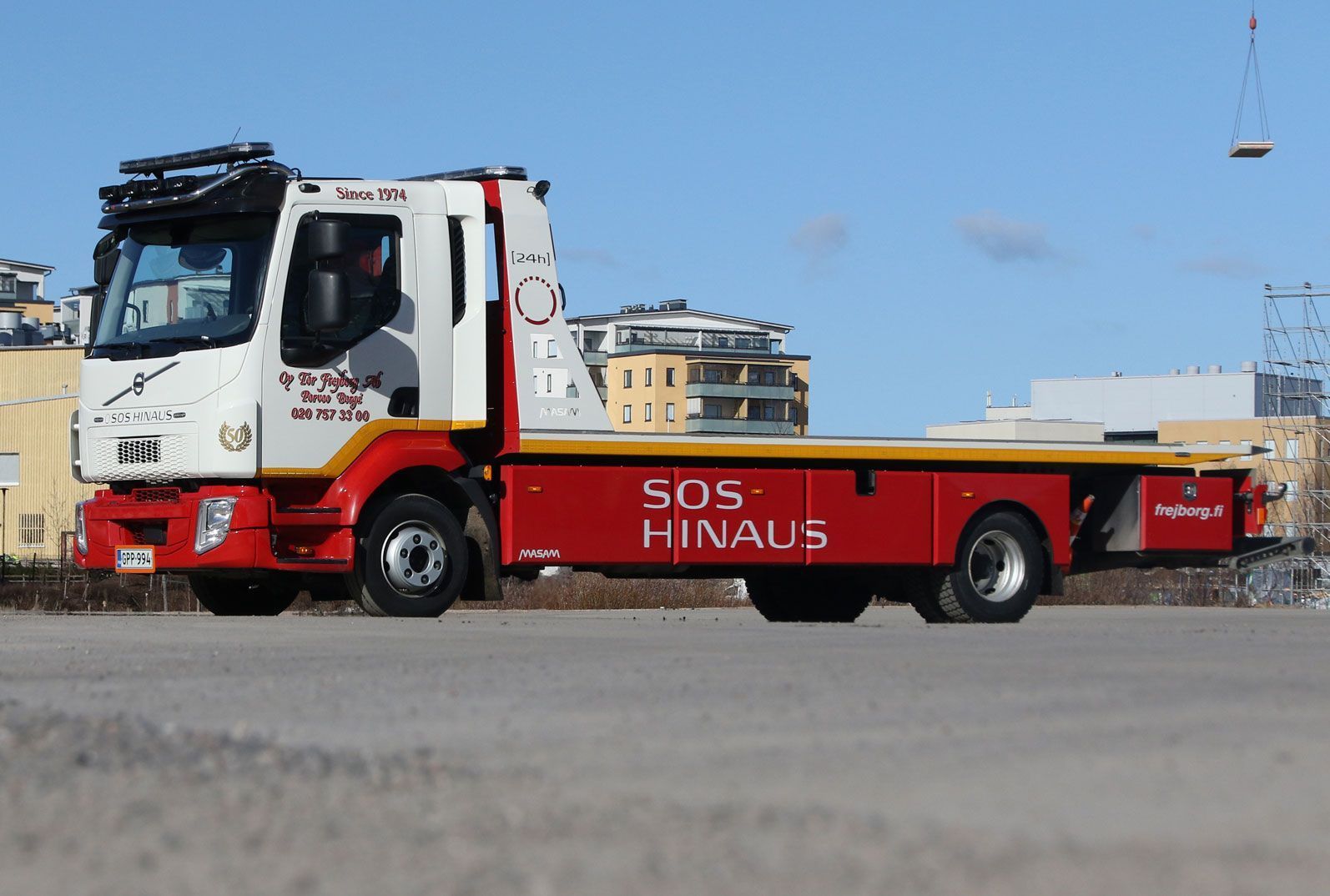 Punainen Hinaus-hinausauto pysäköitynä soratontille rakennusten ja nosturin lähelle