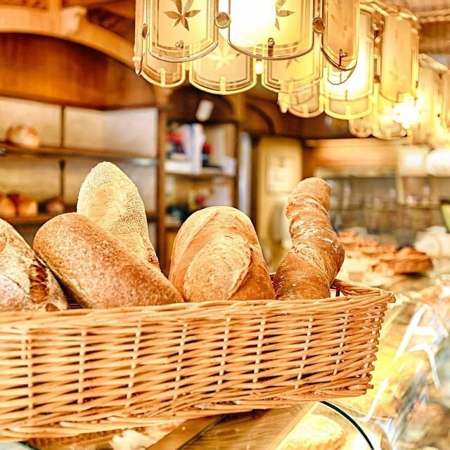 Un panier en osier rempli de pains artisanaux assortis, à l'intérieur d'une boulangerie, avec des guirlandes lumineuses chaleureuses au-dessus.