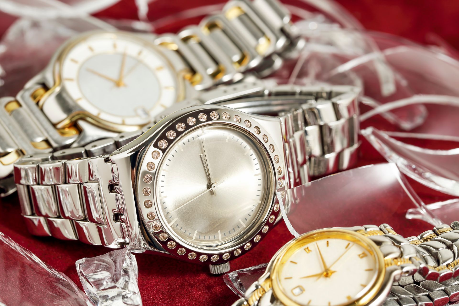 Primer plano de cuatro relojes de pulsera sobre una superficie roja reflectante, con fragmentos de vidrio dispersos.