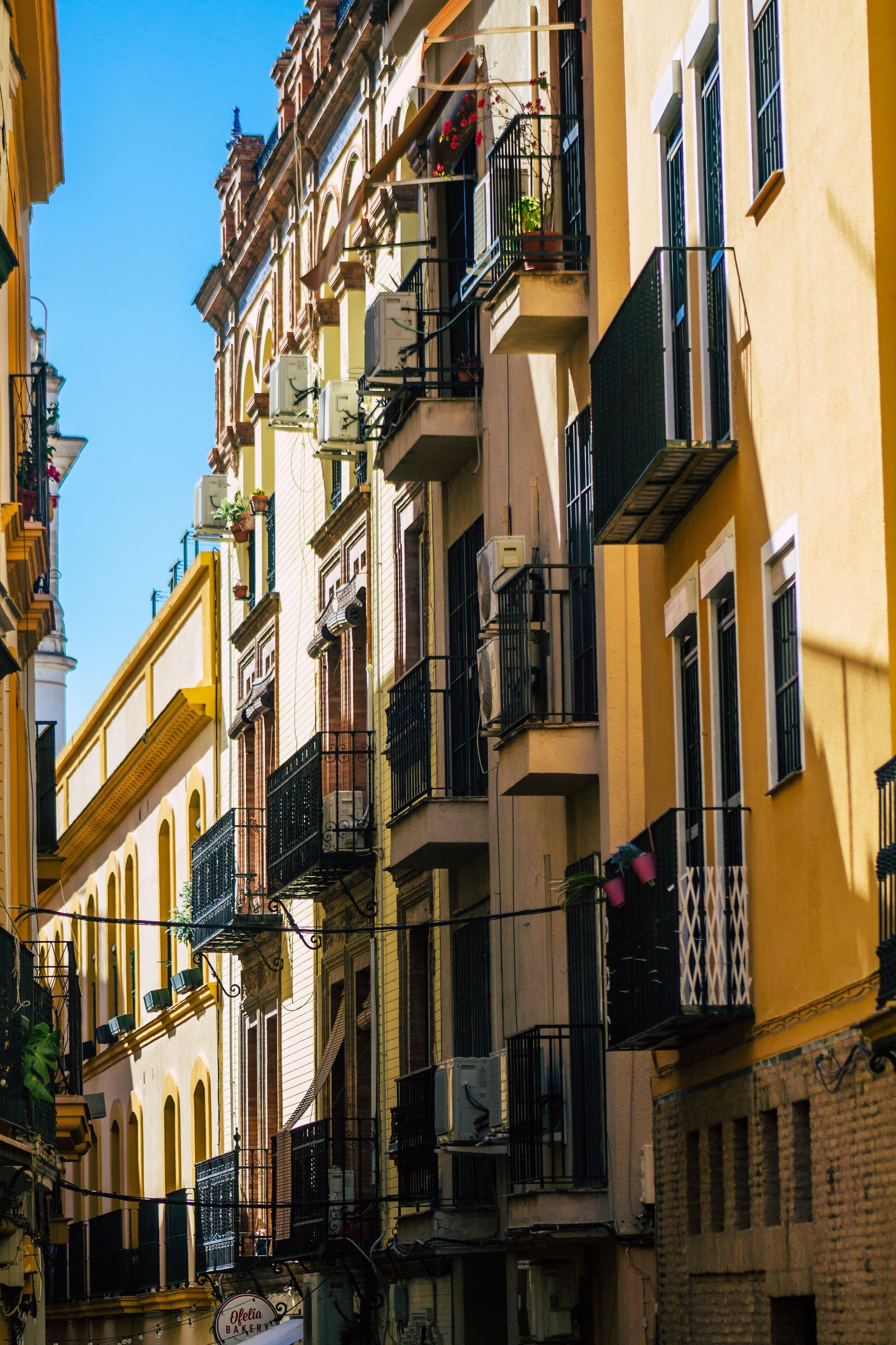 Calle estrecha bordeada de edificios coloridos y ornamentados con balcones en Sevilla, España.